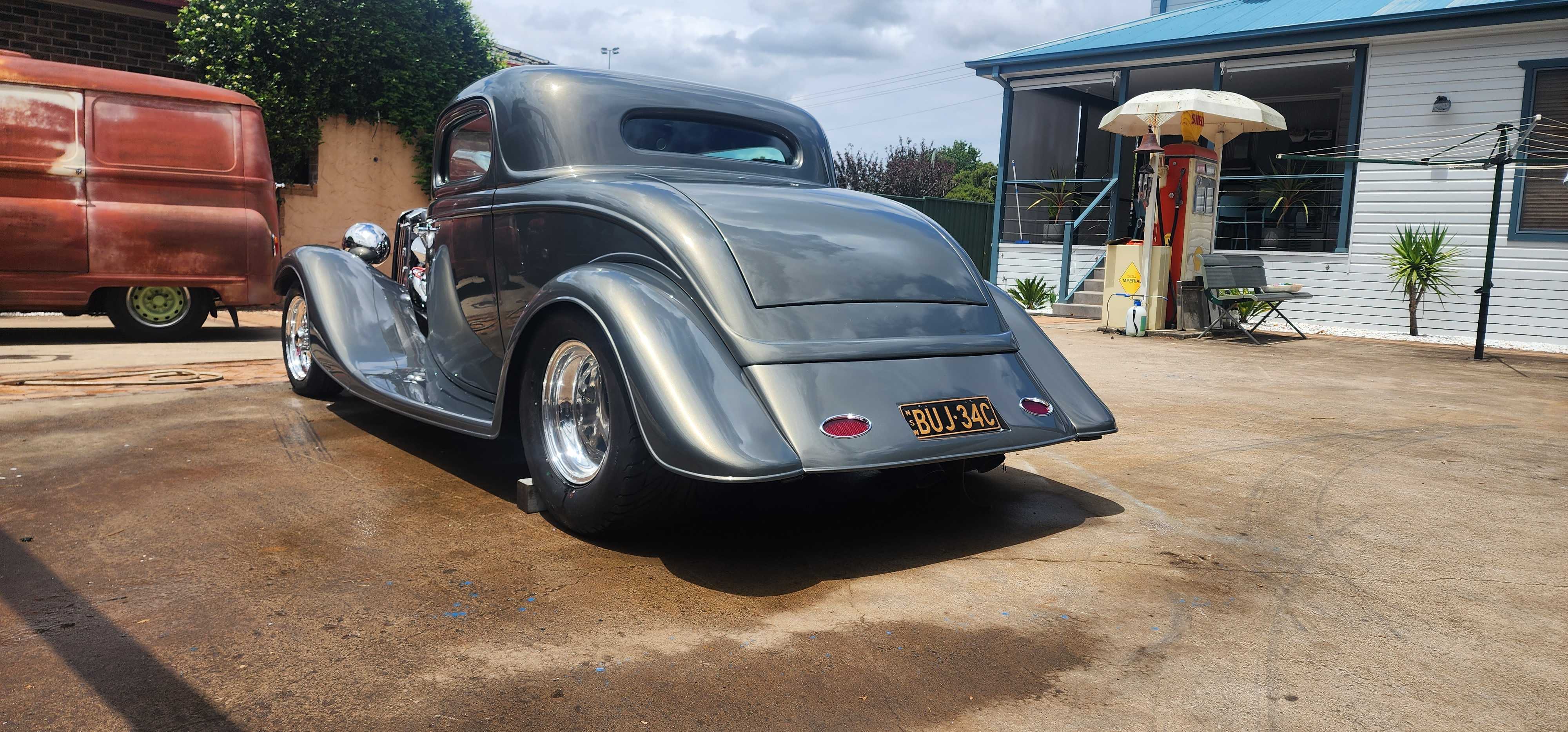 Silver hot rod coupe seen from the rear three quarter, sitting low on polished wheels